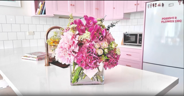 Bouquet of flowers in a kitchen with pink cabinets and a refrigerator.